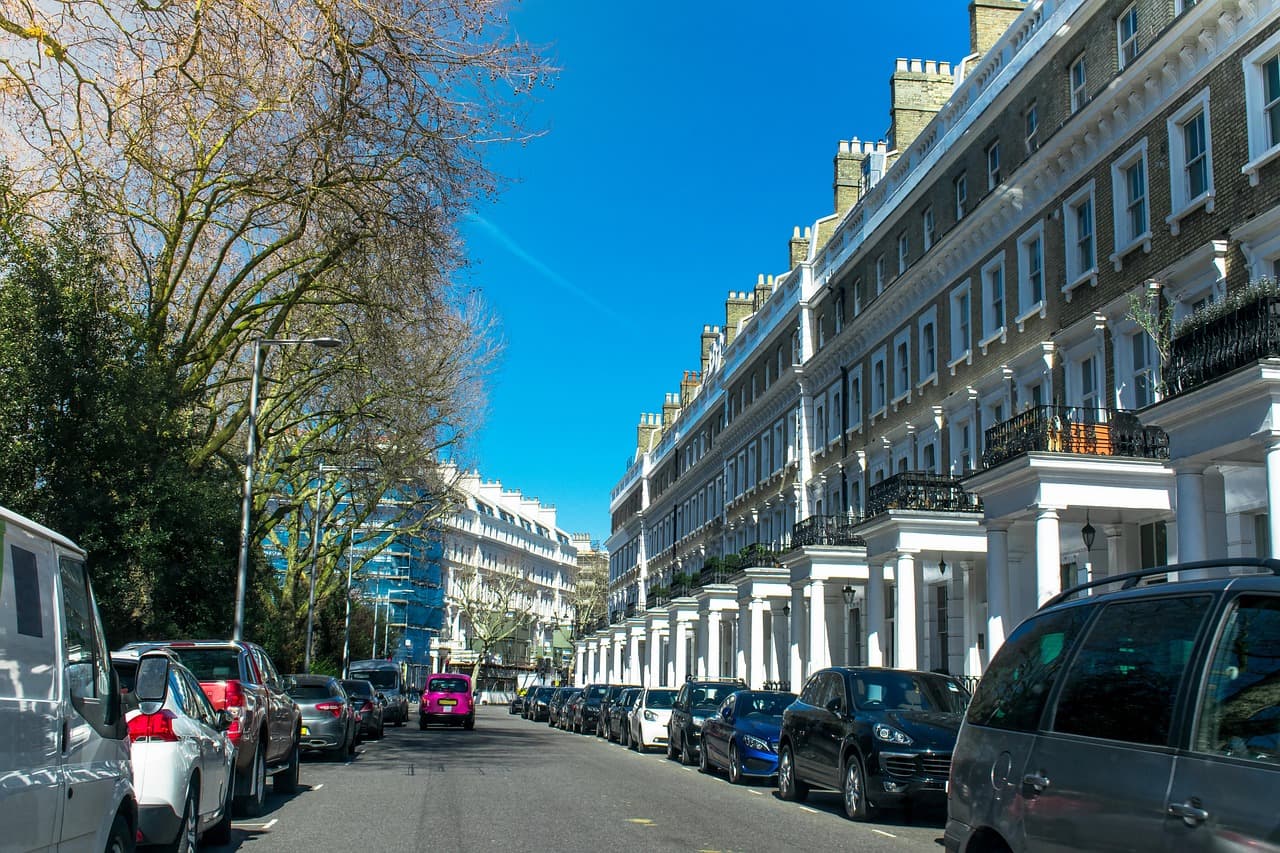 Cars parked along a white stucco terrace on a tree-lined London street